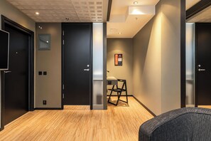 Corredor moderno com portas pretas, uma escrivaninha com cadeira e sinal de saída de emergência fixado na parede.