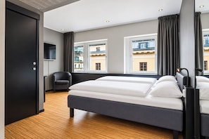 Een moderne hotelkamer met een groot bed, een stoel, een televisie en uitzicht op gebouwen door de ramen.