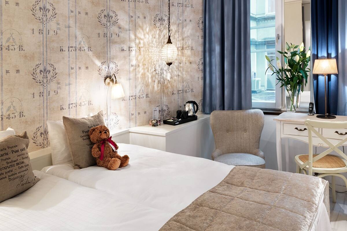 Ein Hotelzimmer mit Bett, Stuhl, Schreibtisch, Lampe und einem fenster mit Vorhängen.