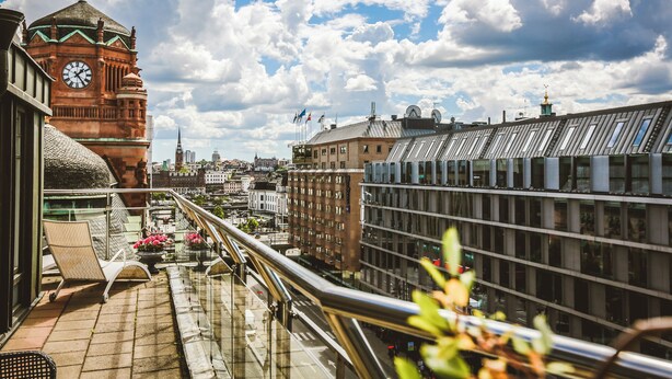 Un balcon offrant une vue sur un beffroi historique et des bâtiments modernes.