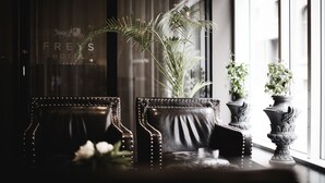 Deux fauteuils en cuir ornés de clous métalliques décoratifs, une plante en pot et un vase rempli de fleurs, le tout posé sur un rebord de fenêtre.
