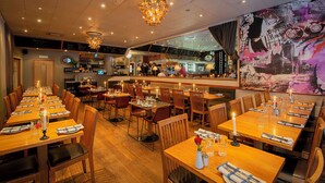 Un restaurant avec des tables et des chaises en bois, un coin bar et une fresque murale.