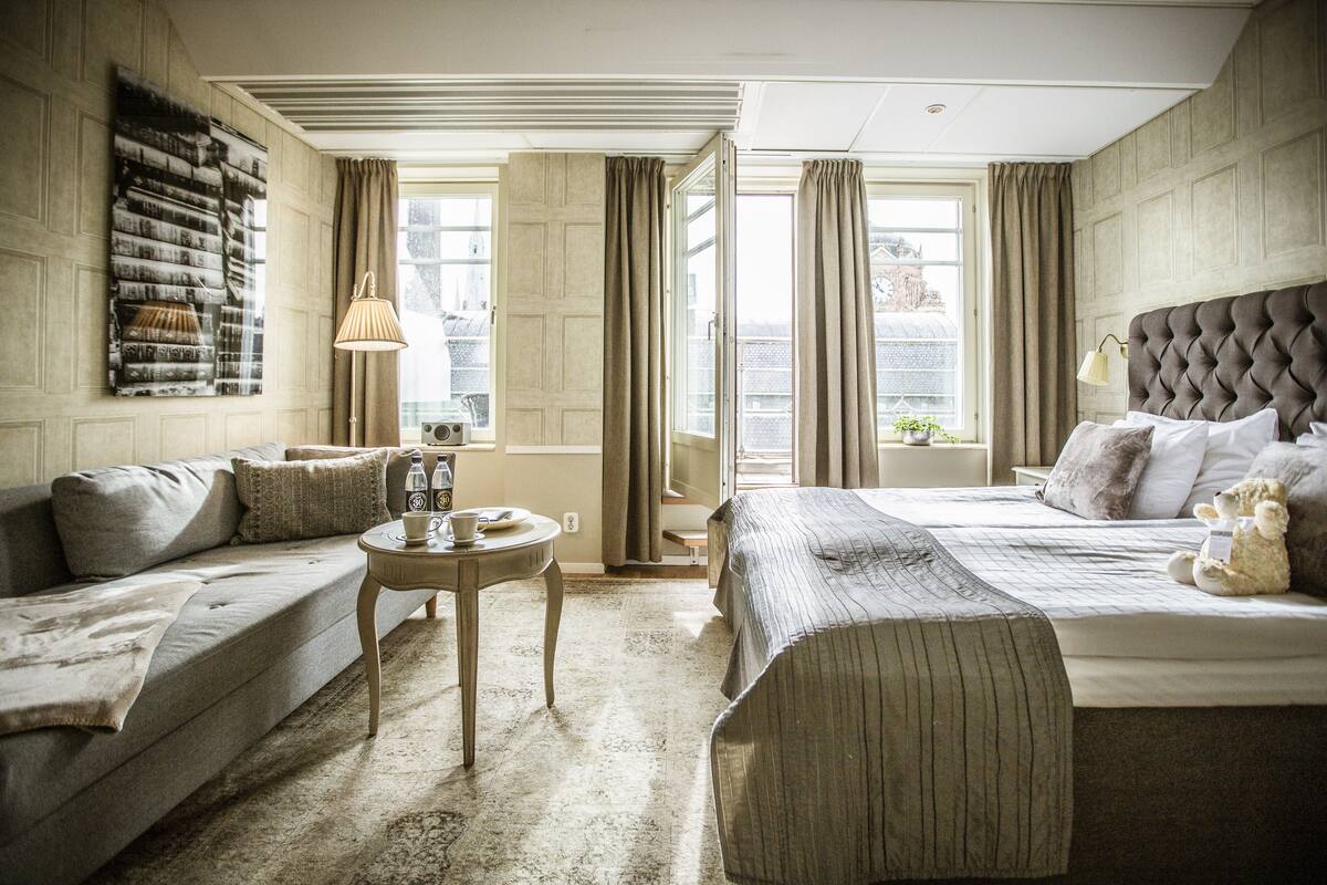 Ein Hotelzimmer mit einem Bett, einer Couch, einem kleinen Tisch und einem Fenster mit Vorhängen.