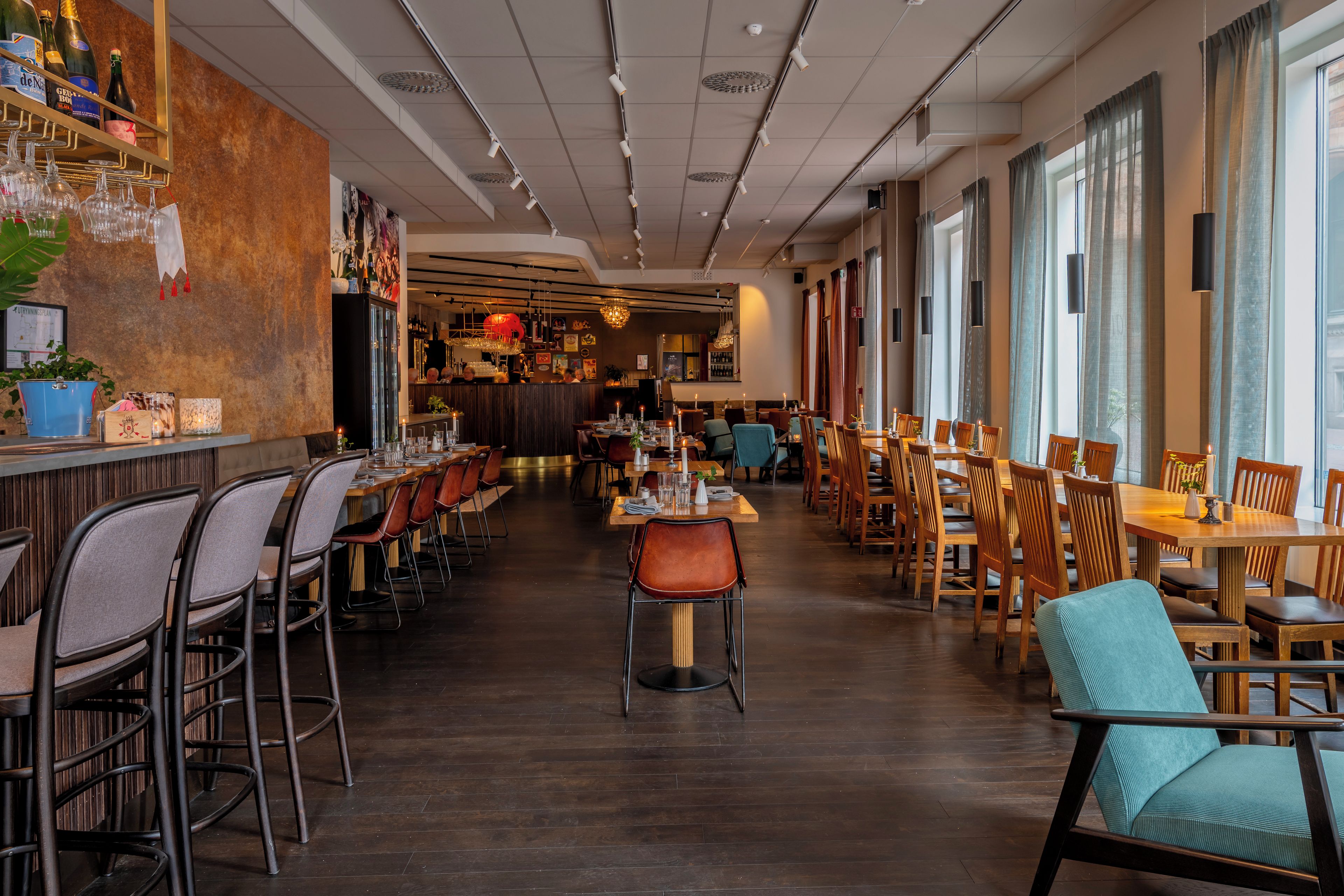 Een restaurant met verschillende eettafels en stoelen, een bar met flessen en uitzicht op de straat door grote ramen.