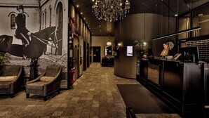 Un hall d’hôtel avec des fauteuils en cuir, un comptoir d’accueil, un lustre et une horloge murale.