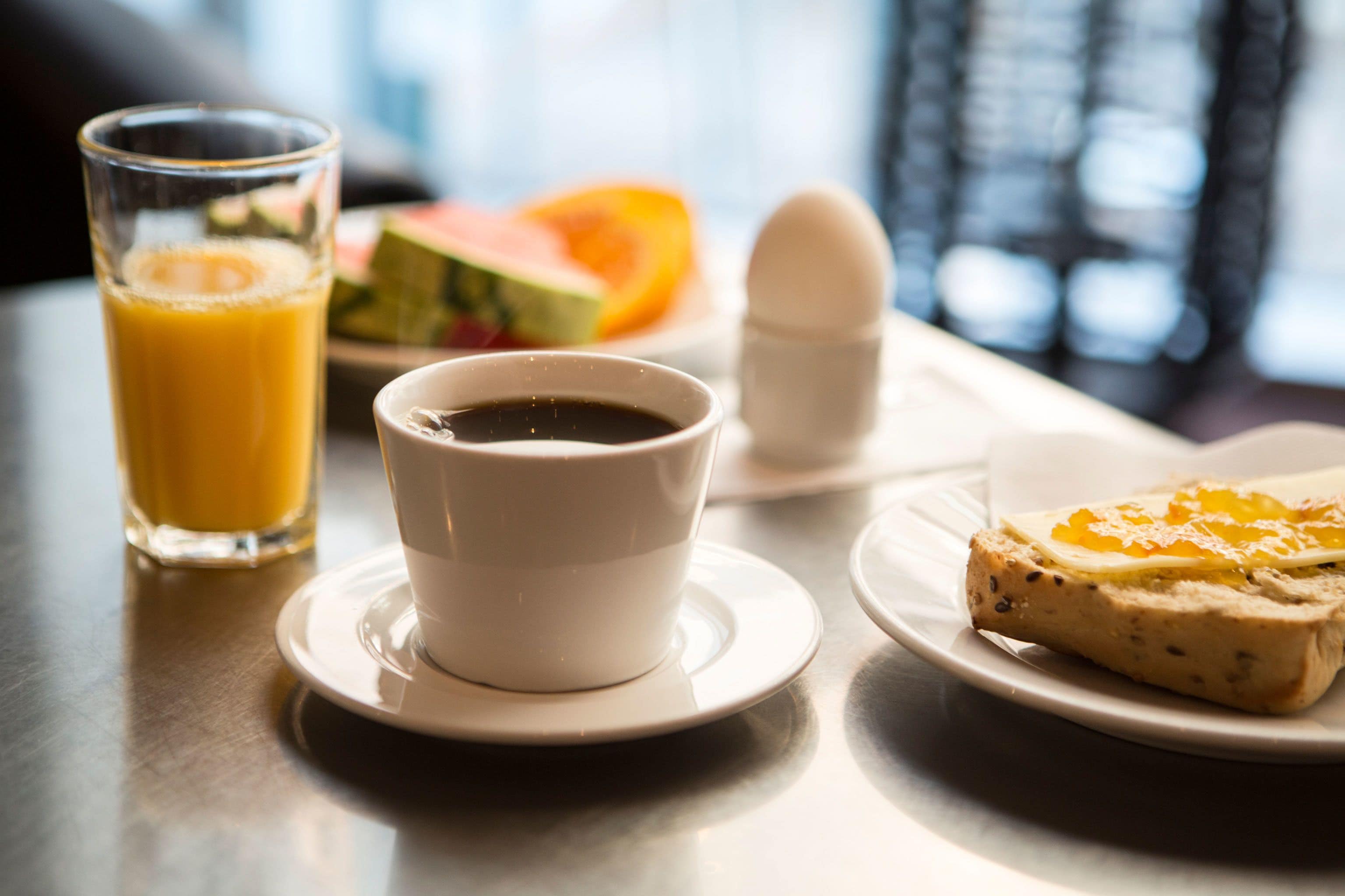A breakfast setting with a glass of orange juice, a cup of coffee, a plate with toast and jam, and a plate with a slice of watermelon.