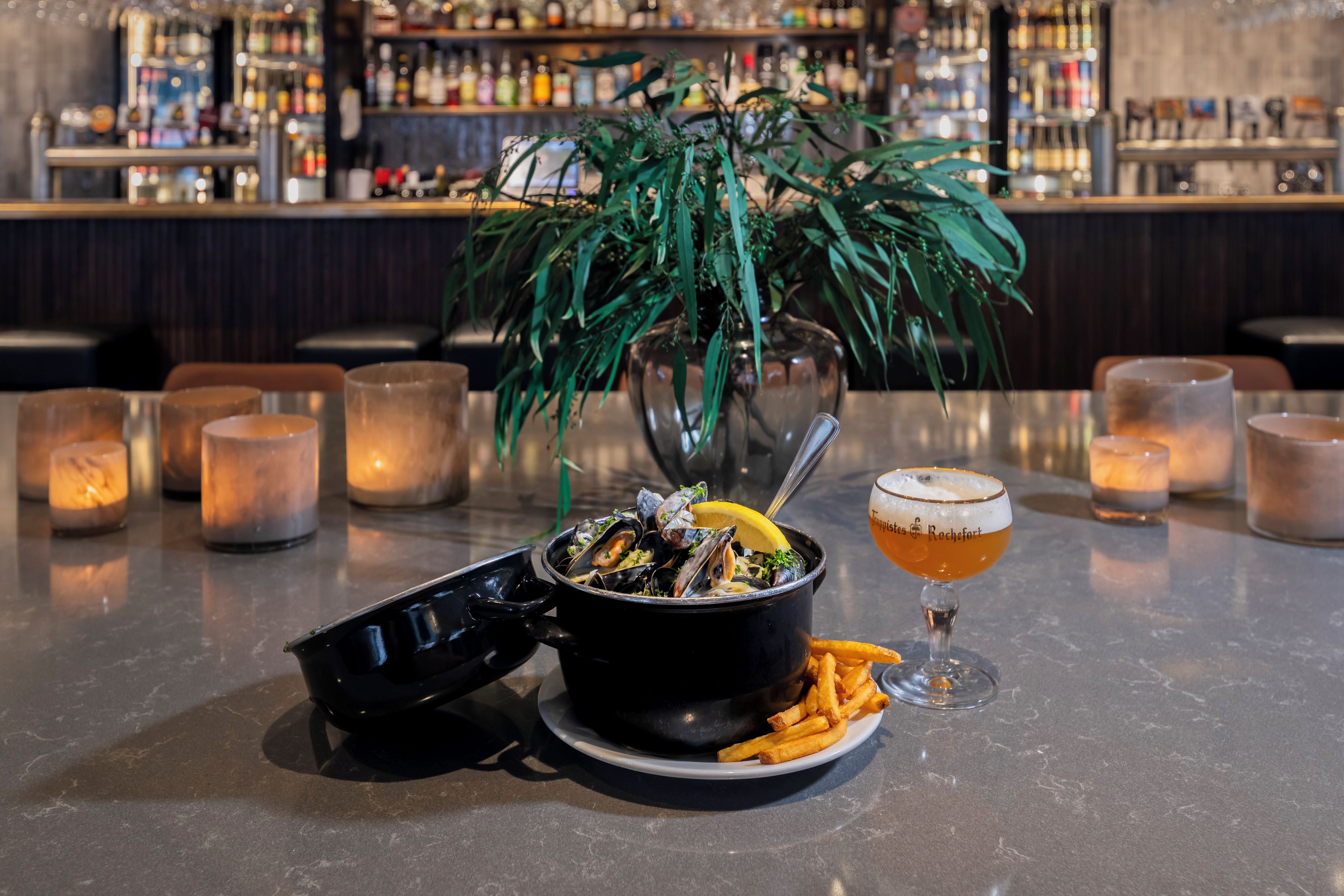 A bar setting with a table set for a meal, including a bowl of mussels, fries, and a glass of beer.