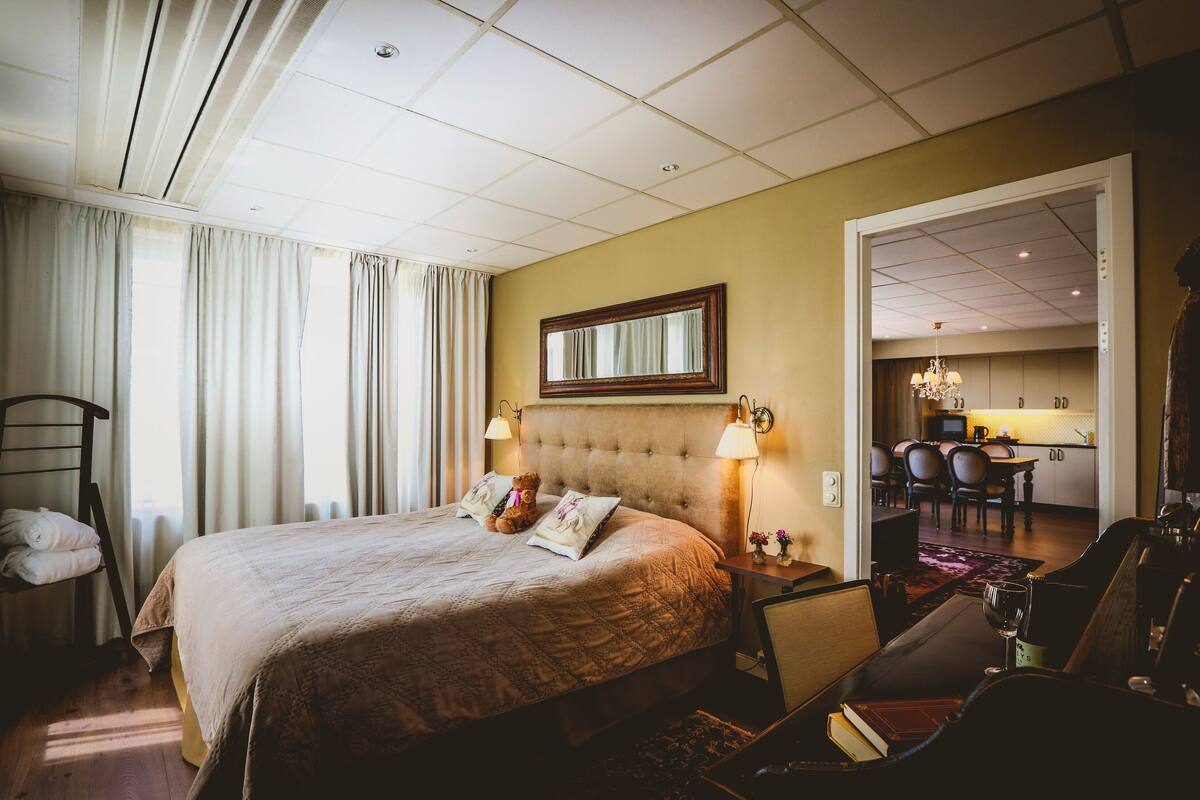Ein Hotelzimmer mit einem großen Bett, einem Schreibtisch, einem Stuhl, einer Lampe und Blick auf den Speisesaal.