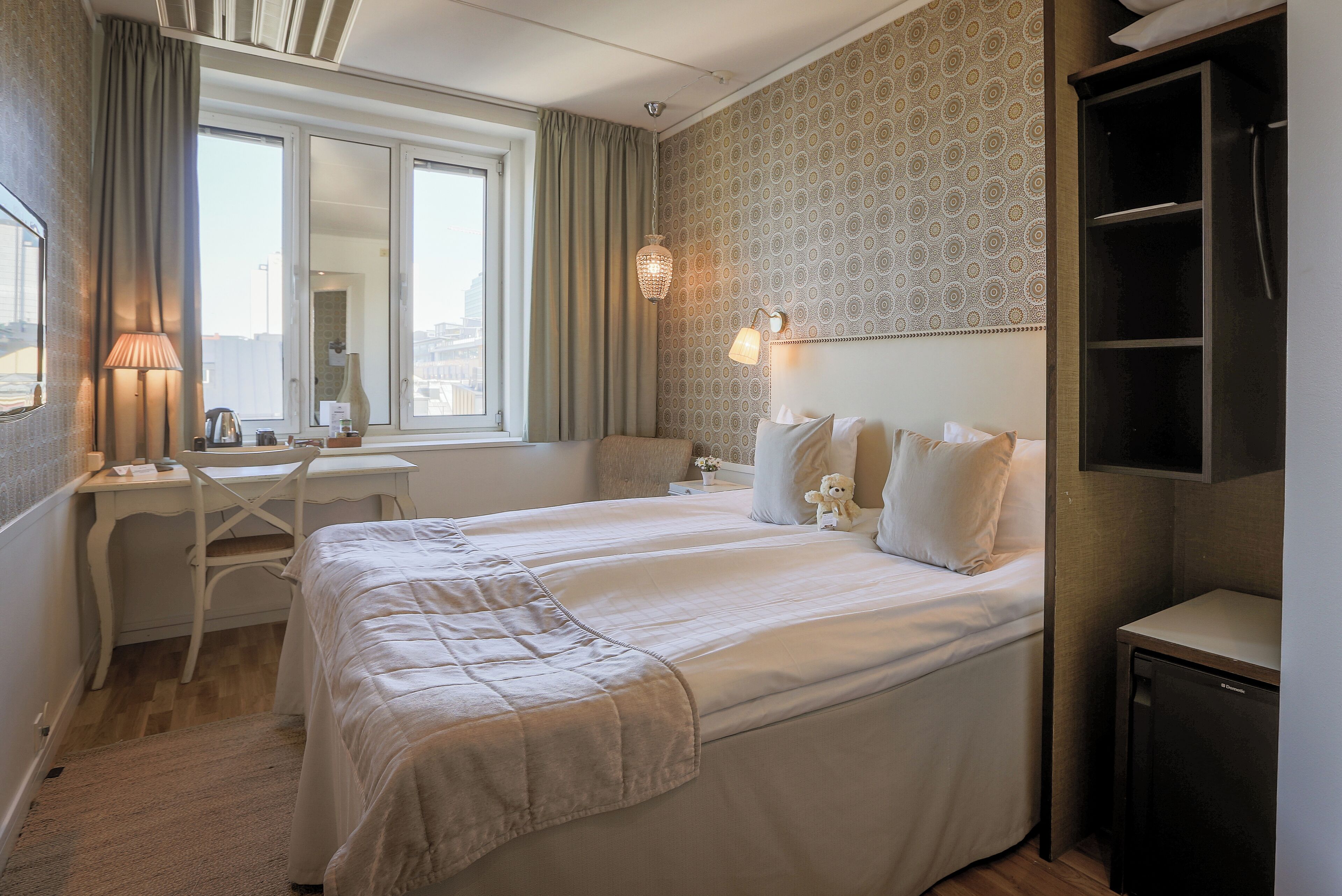 Hotellihuone, jossa on kaksi sänkyä, työpöytä ja tuoli.
