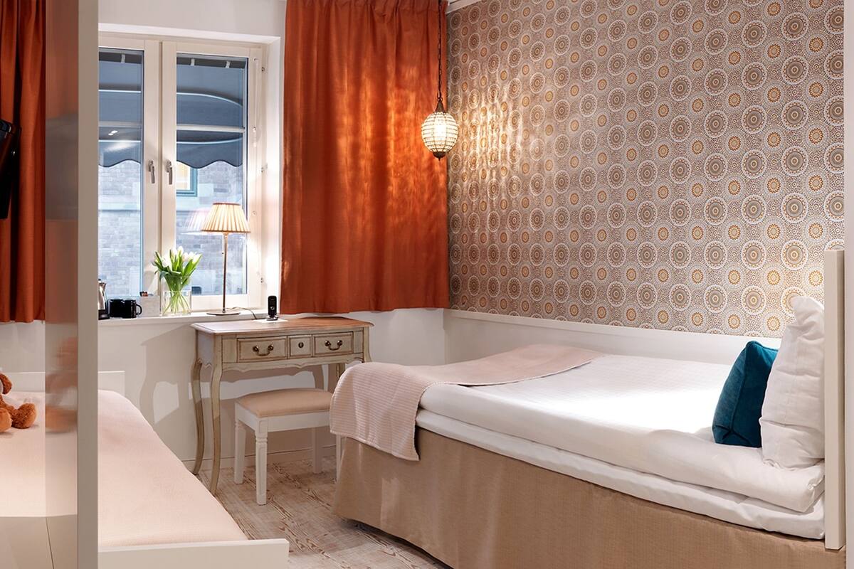 Ein Schlafzimmer mit einem Bett, einem Schreibtisch, einem Stuhl, einem Teddybären und einem Fenster mit Vorhängen.