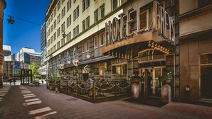 Un hôtel à la façade de style européen classique, doté d’un espace extérieur aménagé et d’une entrée imposante avec une porte en verre.