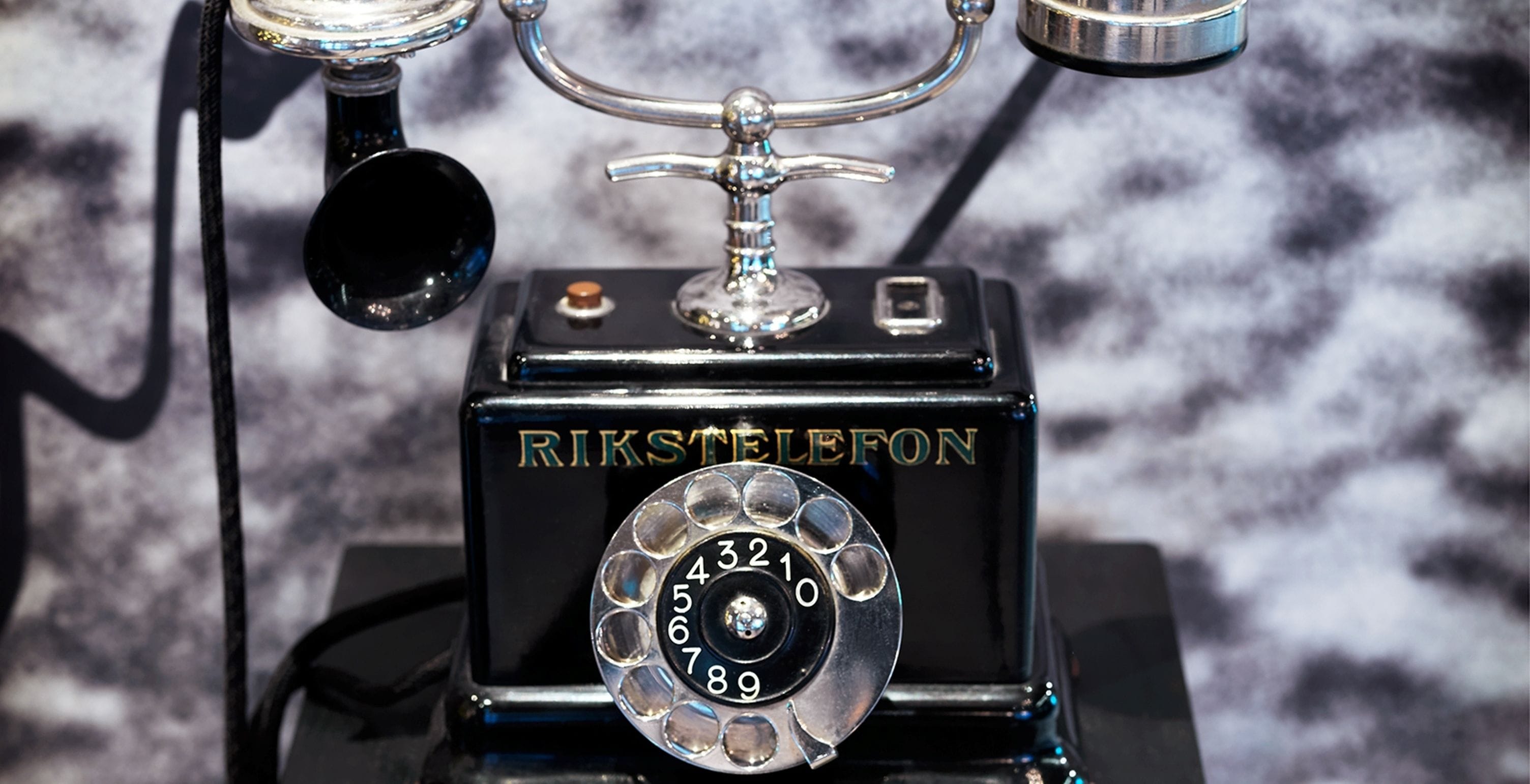 En gammal telefon från RIKSTELEFON med en vridskiva, en sladd och en metallbas.
