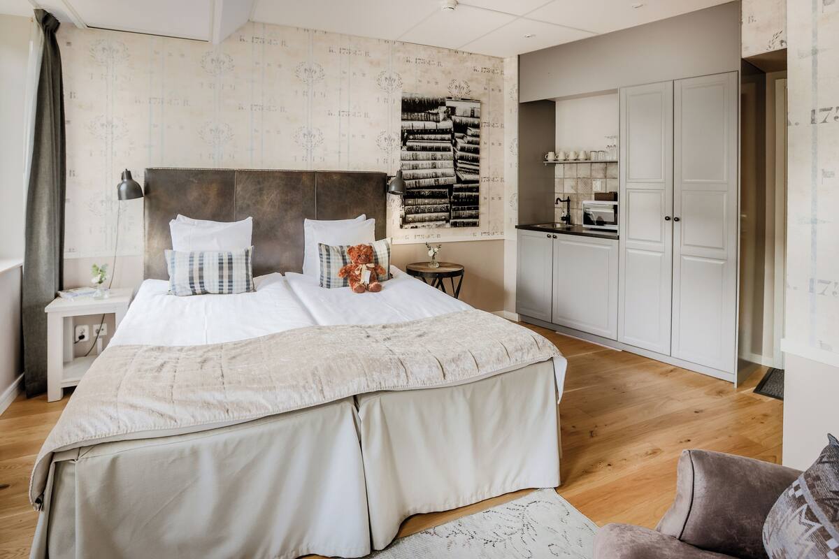 Ein Schlafzimmer mit einem großen Bett, einem Nachttisch, einem kleinen Tisch, einem Kleiderschrank und einer Küchenzeile.