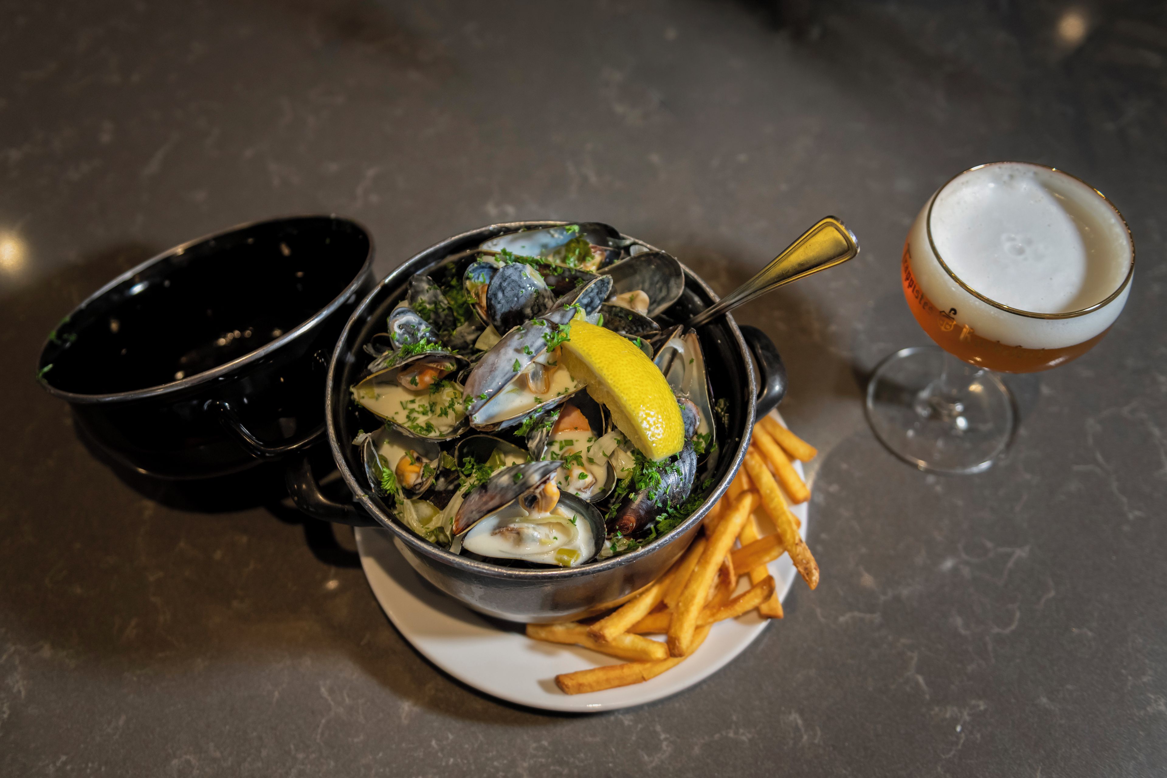 Una ciotola di cozze con limone e prezzemolo, un bicchiere di birra e un piatto di patatine fritte.