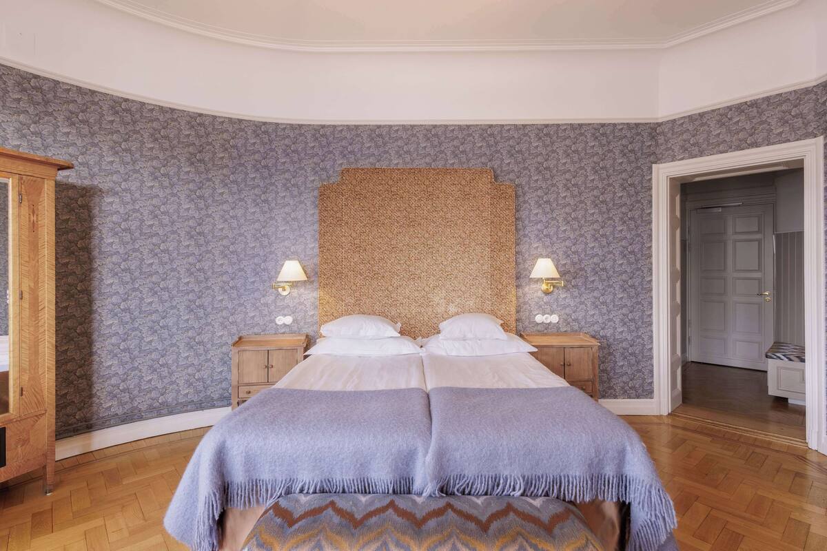 A bedroom with a large bed, two bedside tables with lamps, a wooden wardrobe, and a curved ceiling.