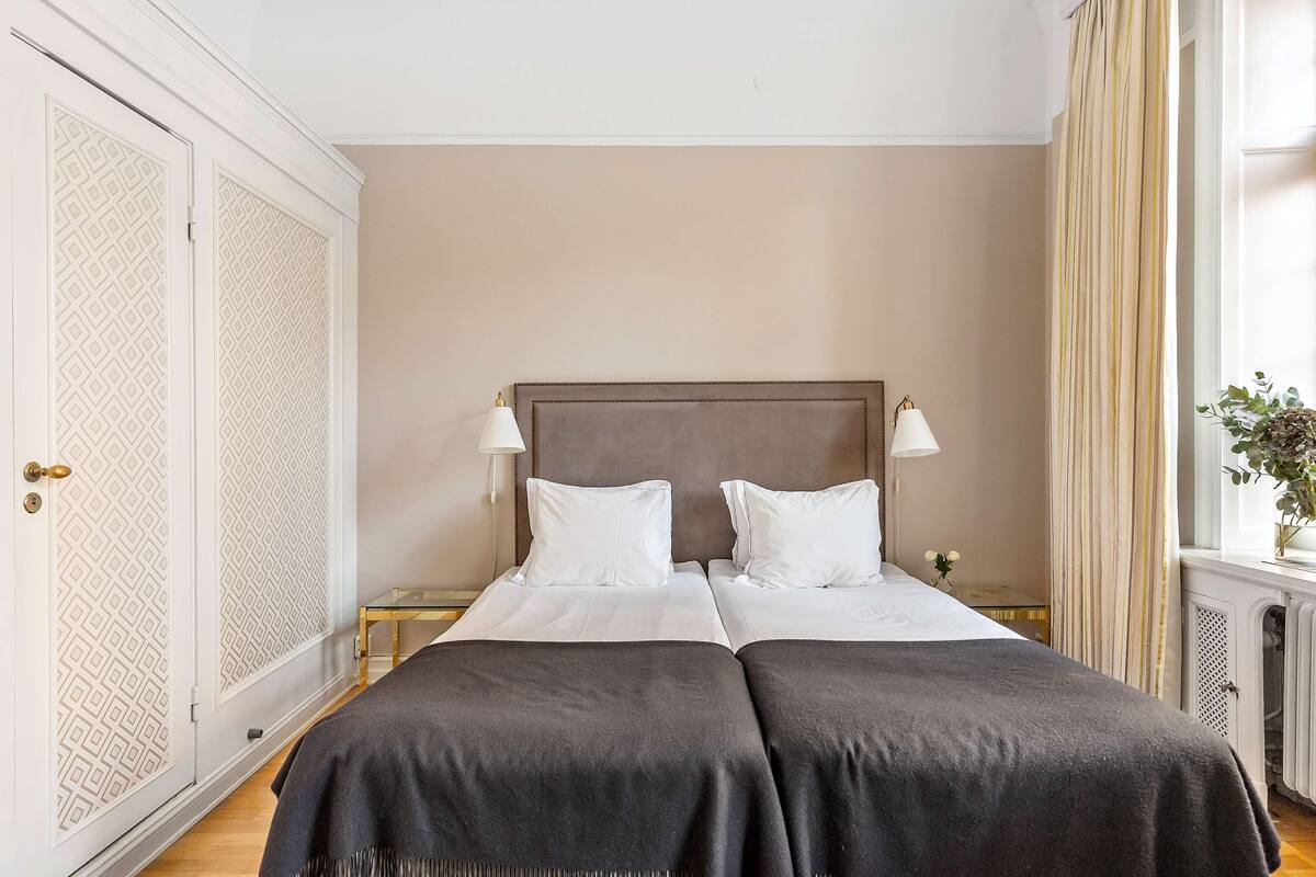 A double bed with two white pillows, a dark throw blanket, and two bedside lamps.