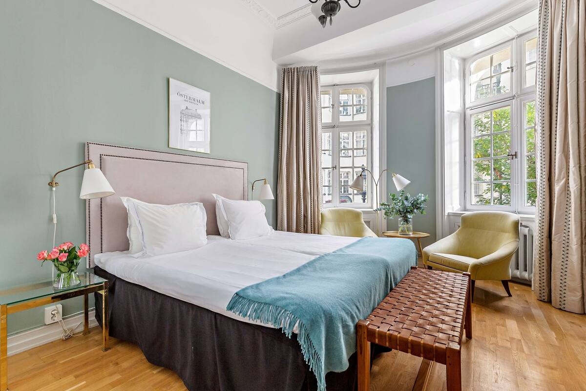 A neatly arranged bedroom with a large bed, bedside lamps, a bench, and a view of the outdoors through a window.