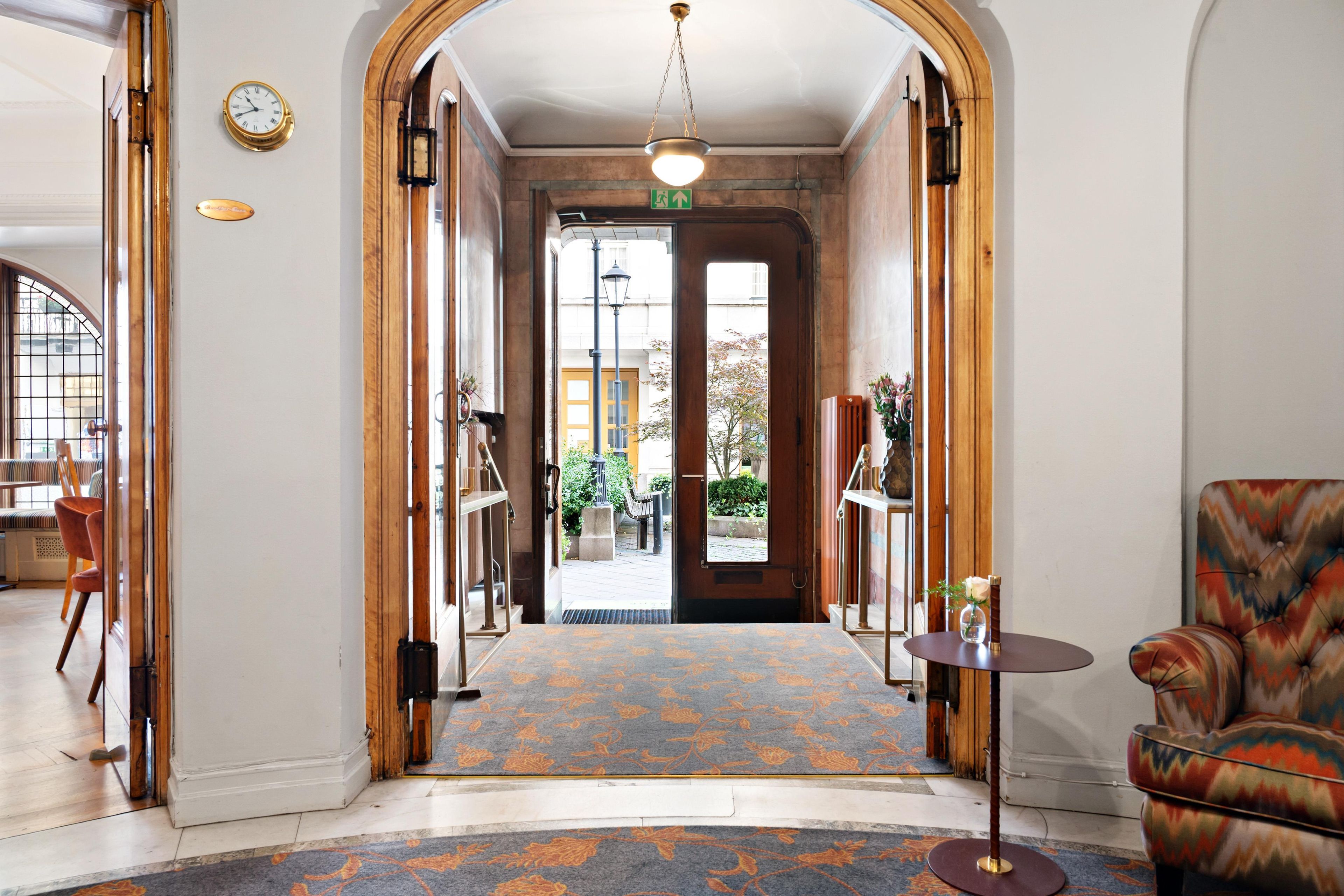 A hotel lobby with a carpeted floor, a reception desk, a chair, and a clock on the wall.