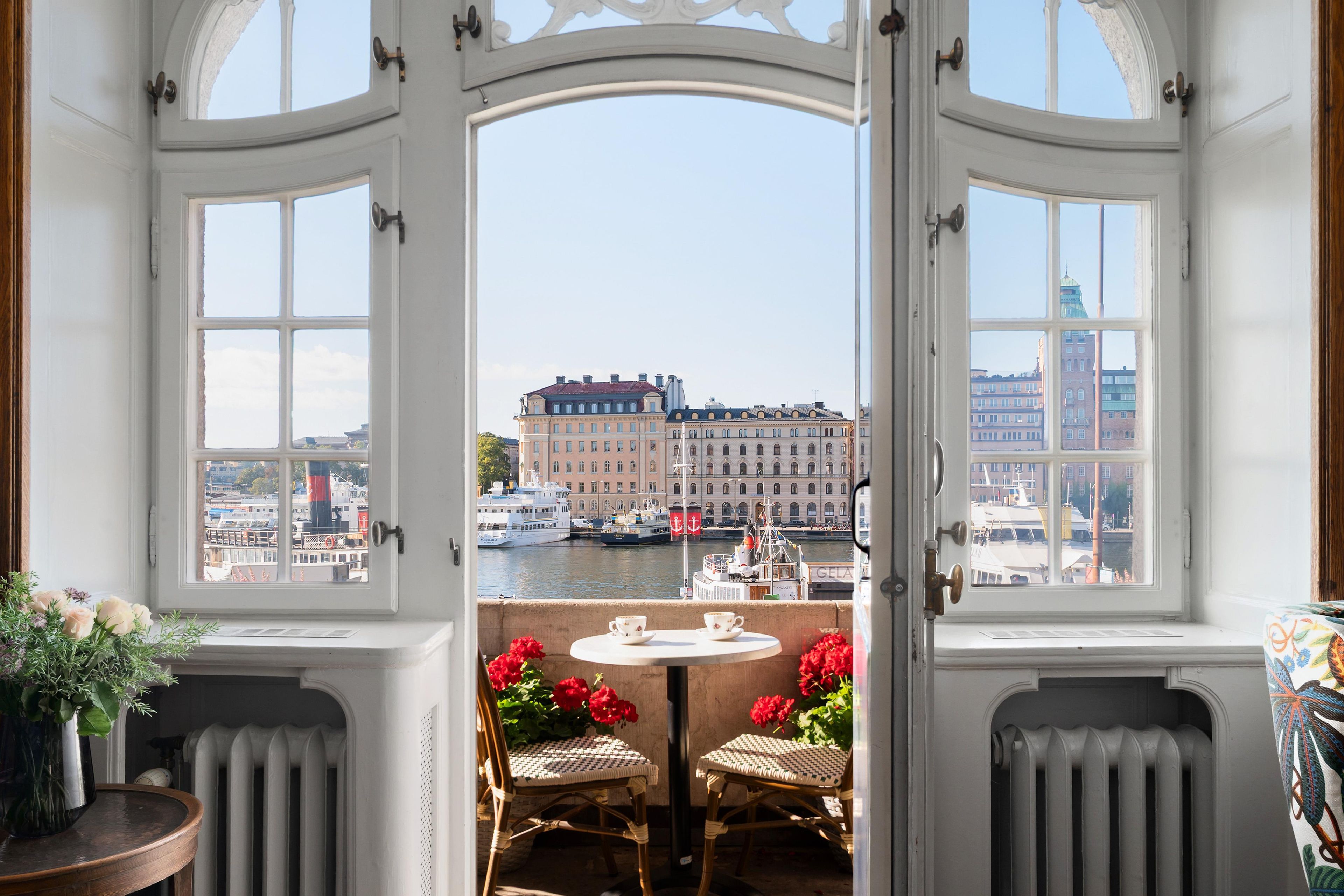 Une pièce avec vue sur un port, comprenant une table avec une tasse et une soucoupe, une chaise et un vase rempli de fleurs.
