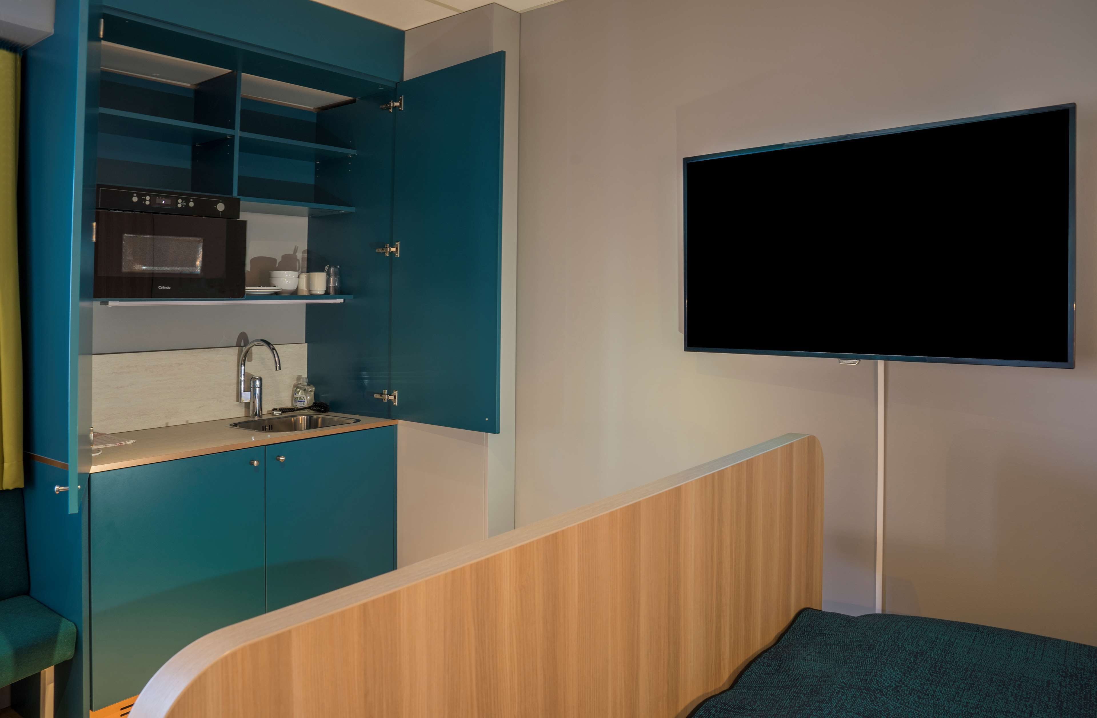 A compact room with a kitchenette, a bed, and a mounted TV.