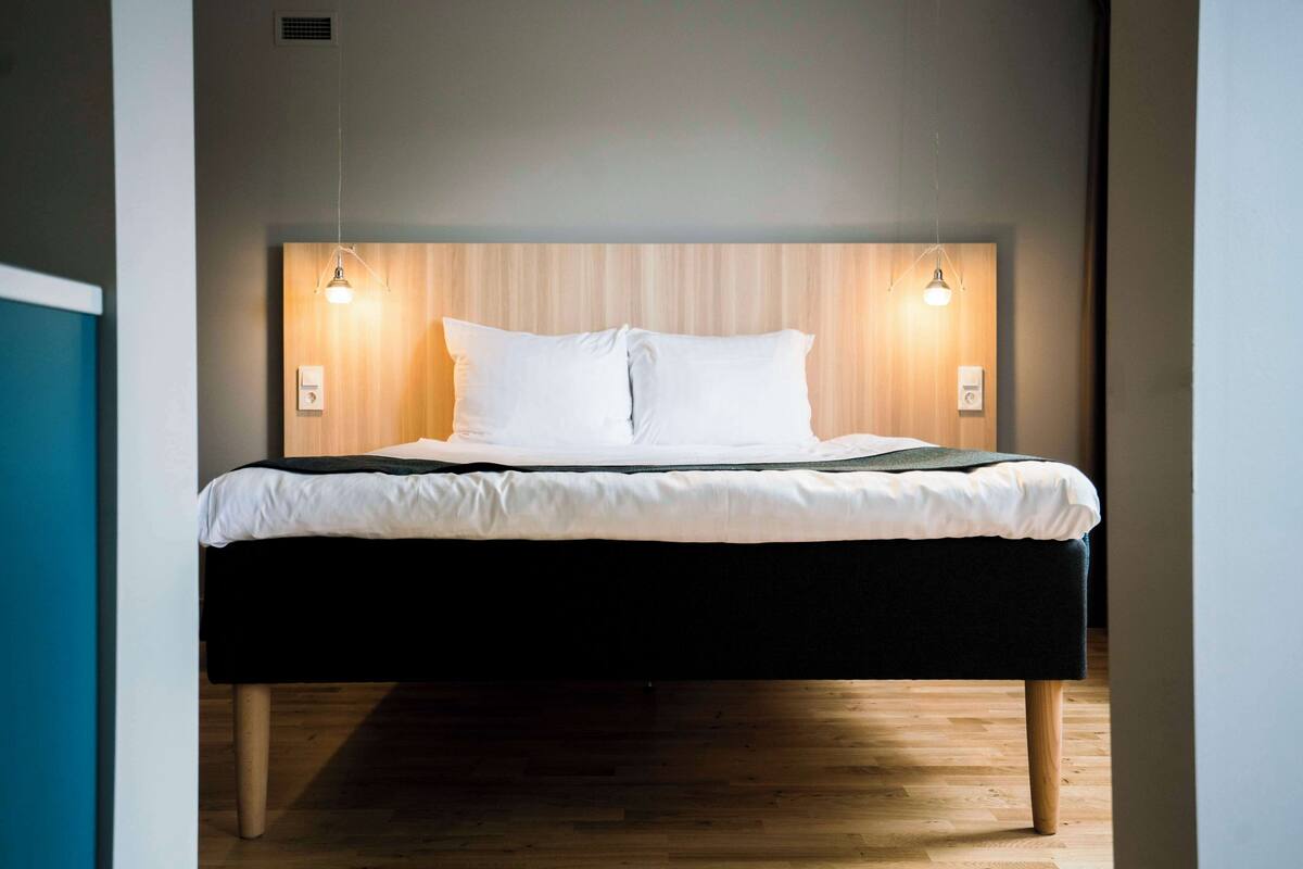 Ein modernes Schlafzimmer mit einem Holzkopfteil, zwei Nachttischlampen und einem ordentlich bezogenen Bett.