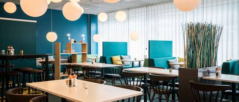 A modern restaurant with round tables, blue and green seating, and hanging spherical lights.