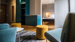 A modern hotel room with a sofa, ottoman, and a bed with a wooden headboard. - Scandic Kista (Kista)