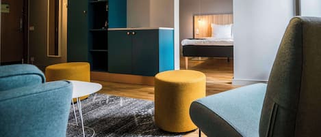 Una habitación de hotel moderna con sofá, reposapiés y una cama con cabecera de madera.