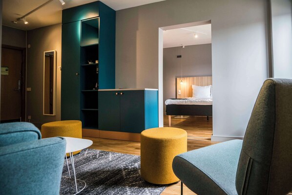 A modern hotel room with a sofa, ottoman, and a bed with a wooden headboard. - Scandic Kista (Kista)