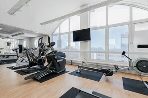 A gym with cardio machines, a rowing machine, and a large window with a view of the city. - Memory Hotel (Kista)