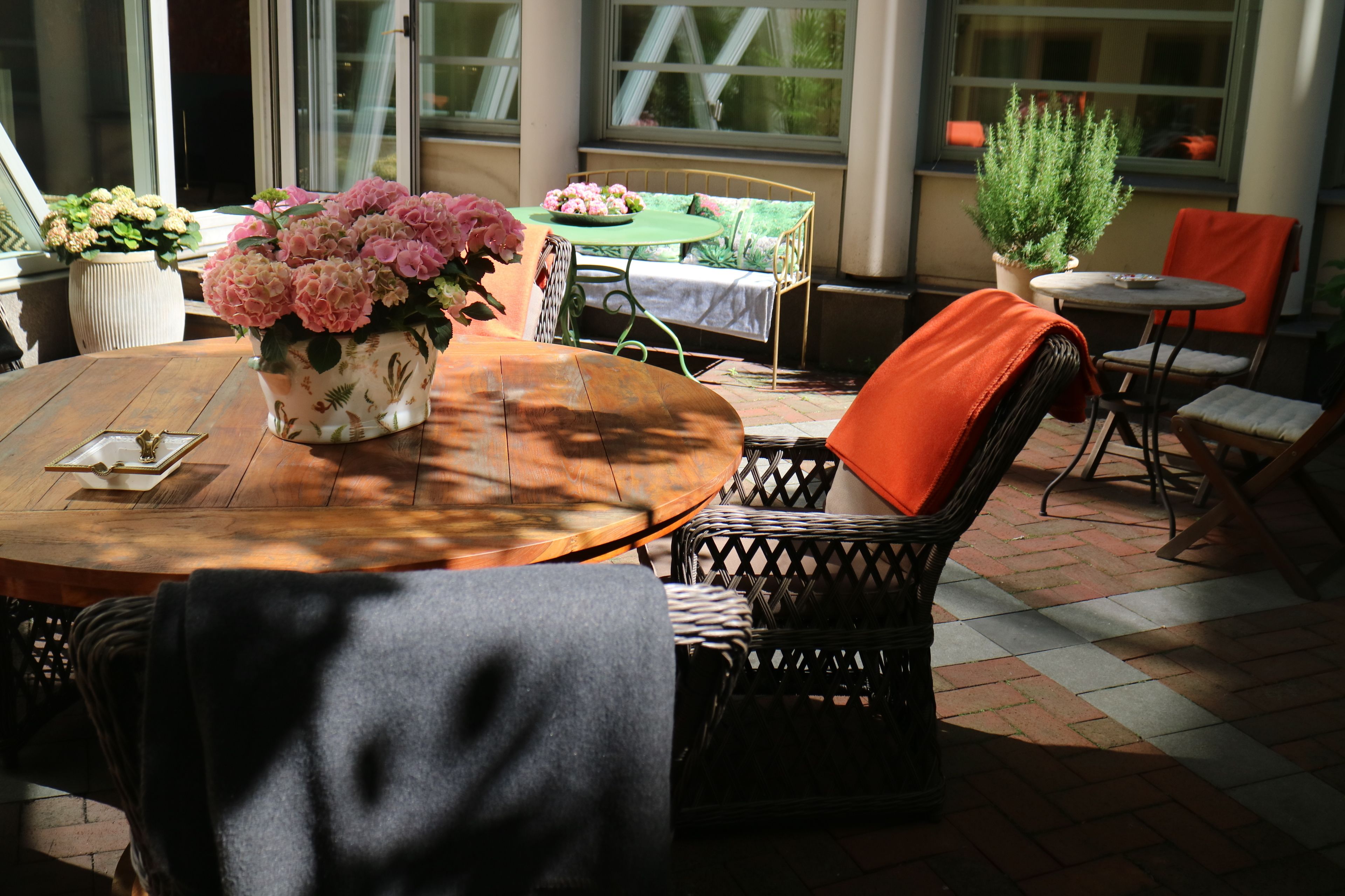 A cozy outdoor seating area with a round wooden table, wicker chairs, and a potted plant.