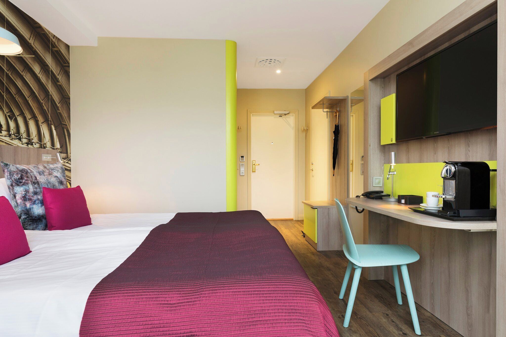 A hotel room with a bed, a desk, a chair, a television, and a coffee machine.