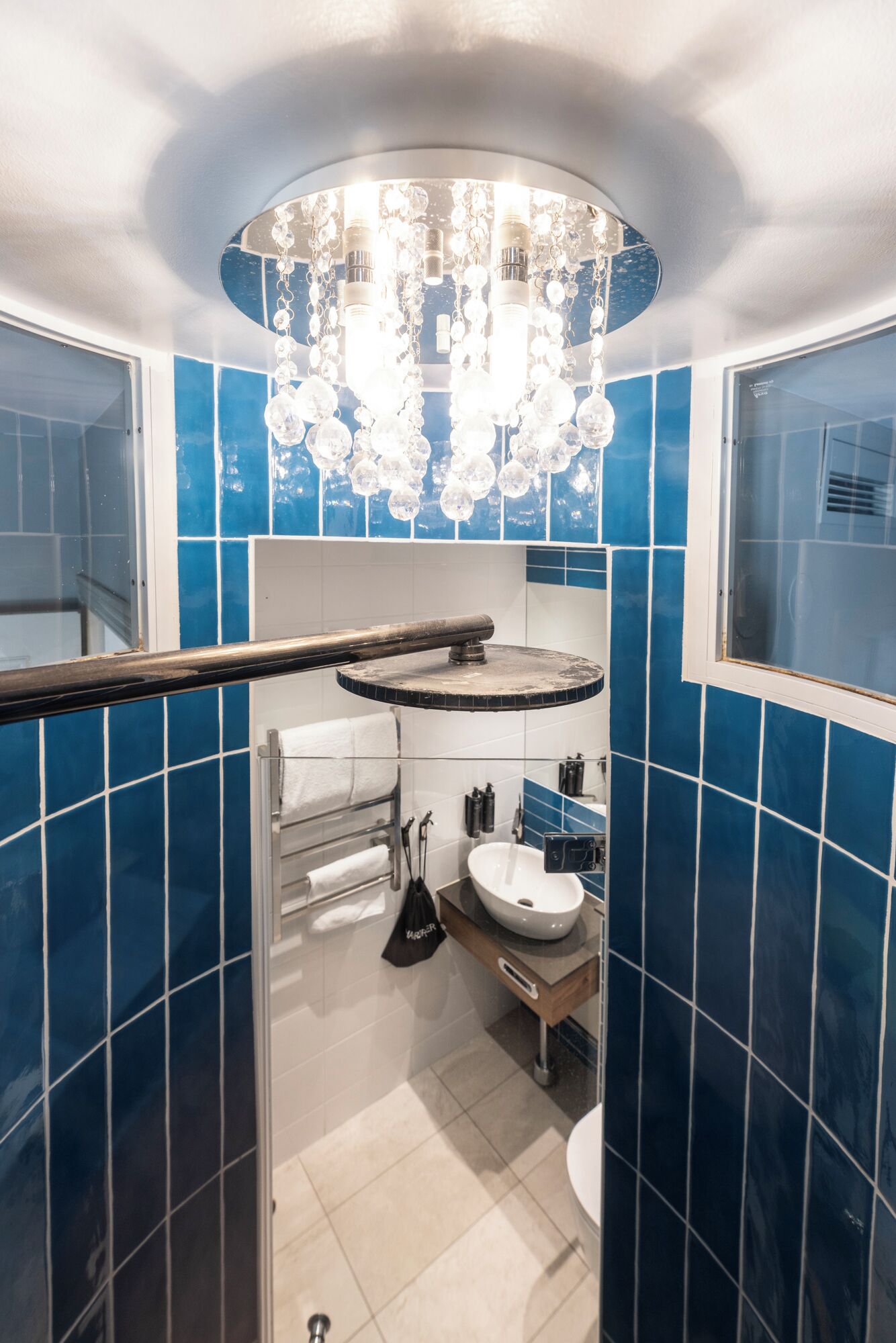 Une salle de bain avec des carreaux bleus, un lavabo blanc et un lustre.