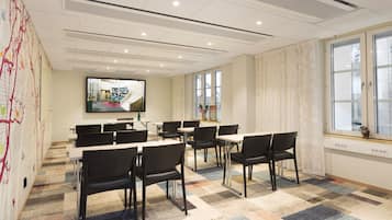 A conference room with a large screen, multiple tables, and chairs.
