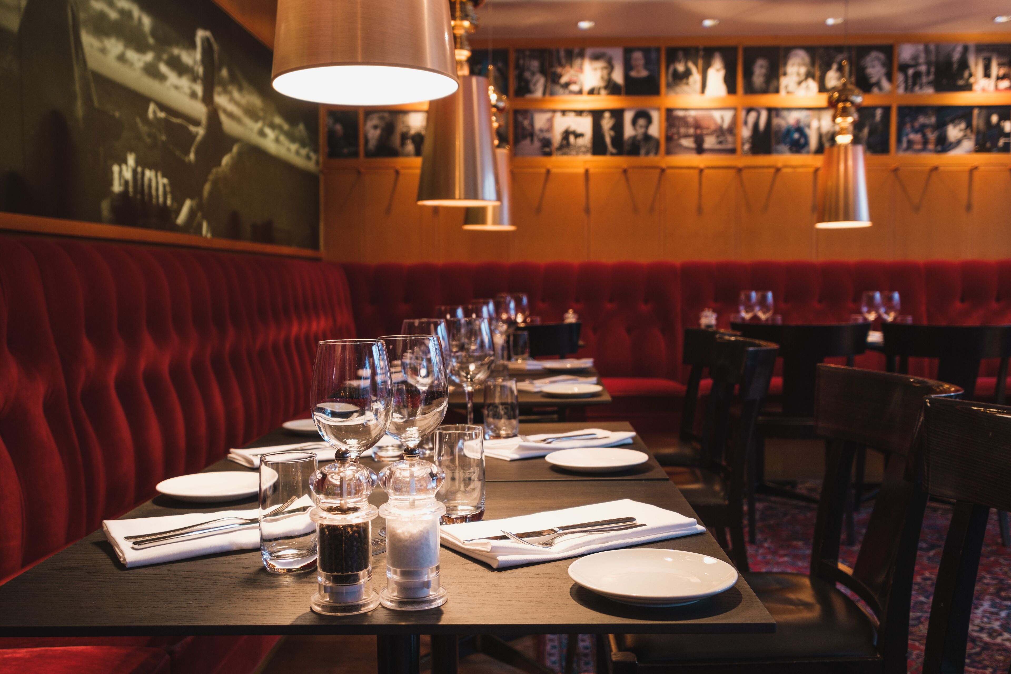 A restaurant with a long table set for dining, red upholstered booths, and framed pictures on the wall.