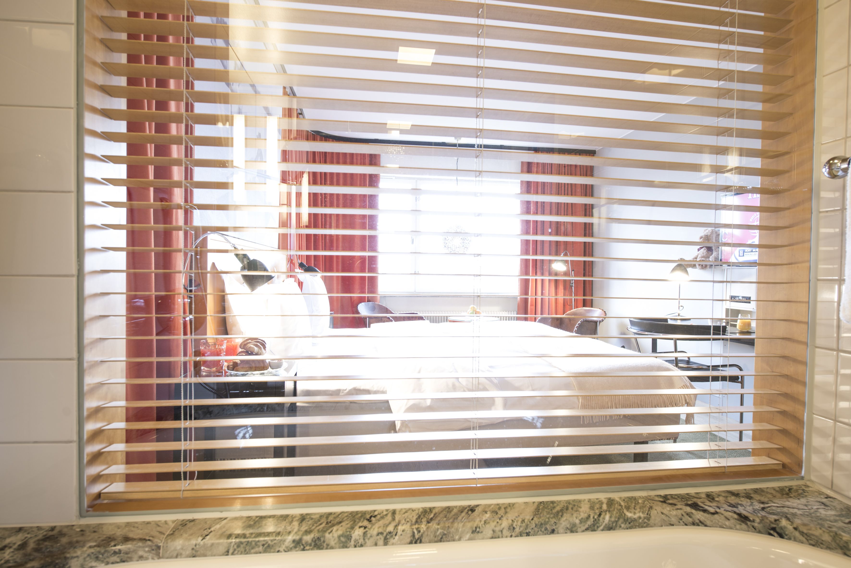 A hotel room with a bed, a desk, a chair, a lamp, and a window with blinds.