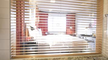 A hotel room with a bed, a desk, a chair, a lamp, and a window with blinds.