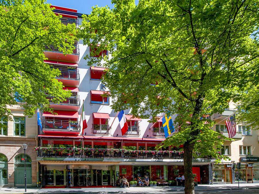 A multi-story building with balconies, a café on the ground floor, and flags.