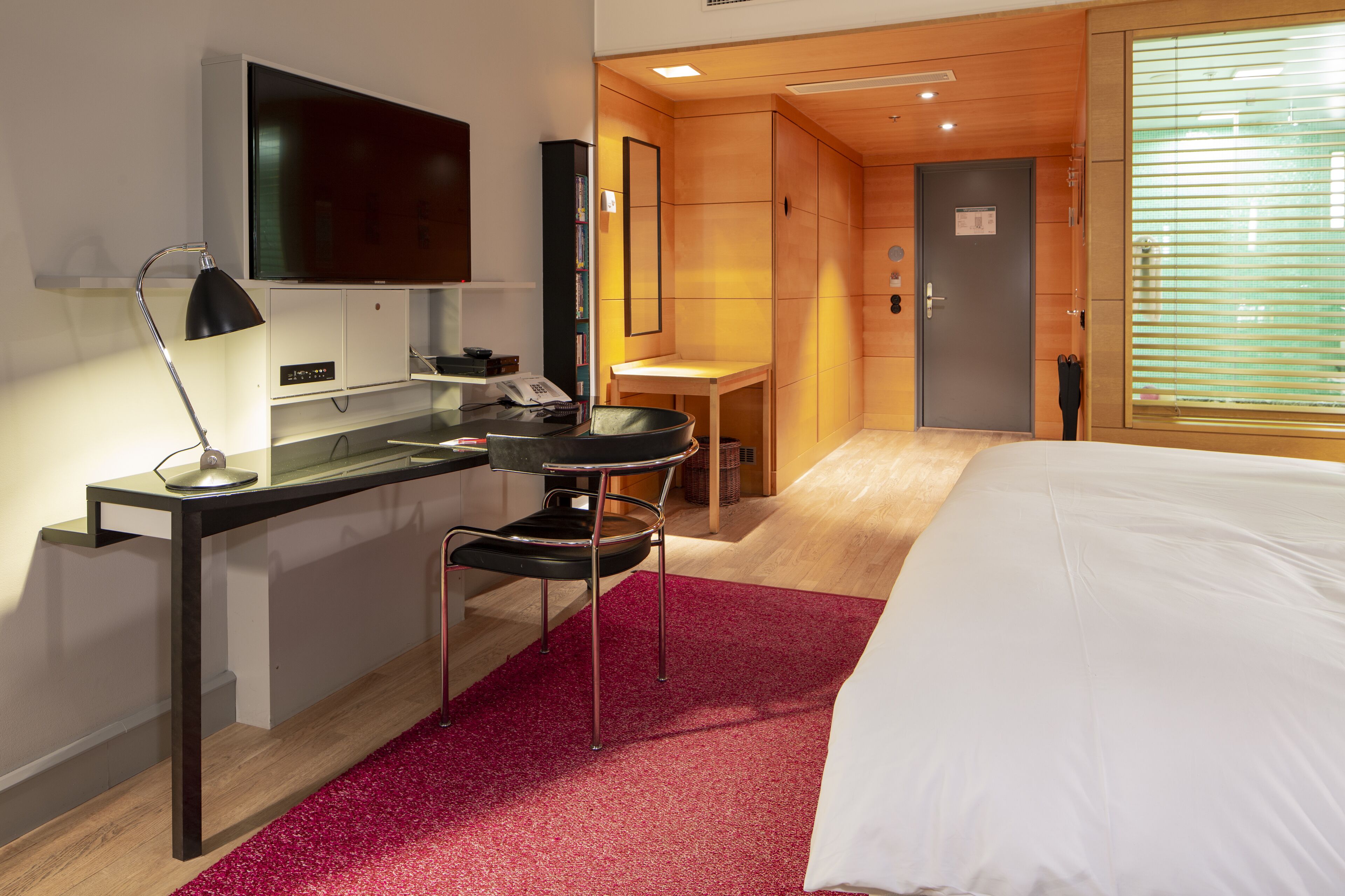 A hotel room with a bed, desk, chair, TV, and a small table.