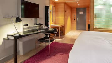 A hotel room with a bed, desk, chair, TV, and a small table.