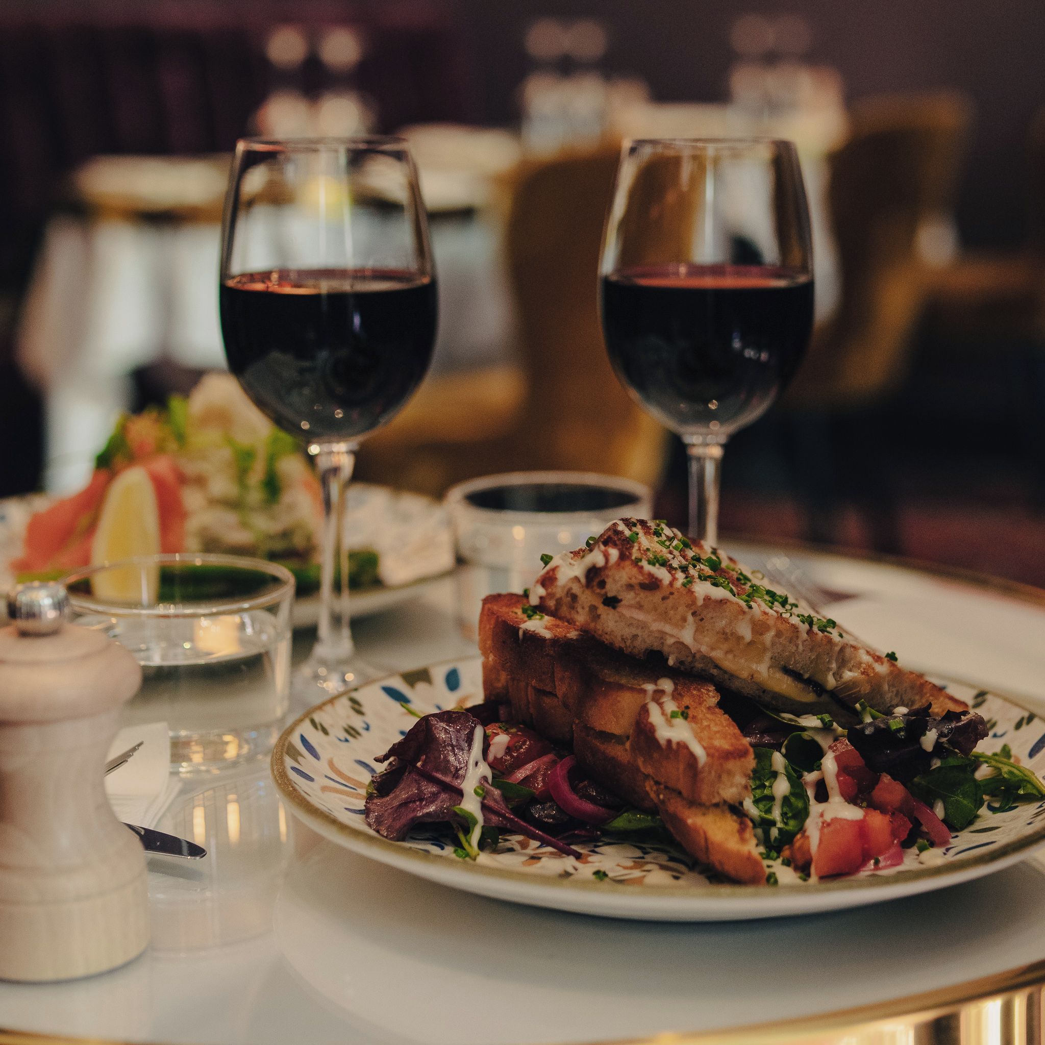 A dining table with a plate of food, two glasses of red wine, and a salt and pepper shaker.