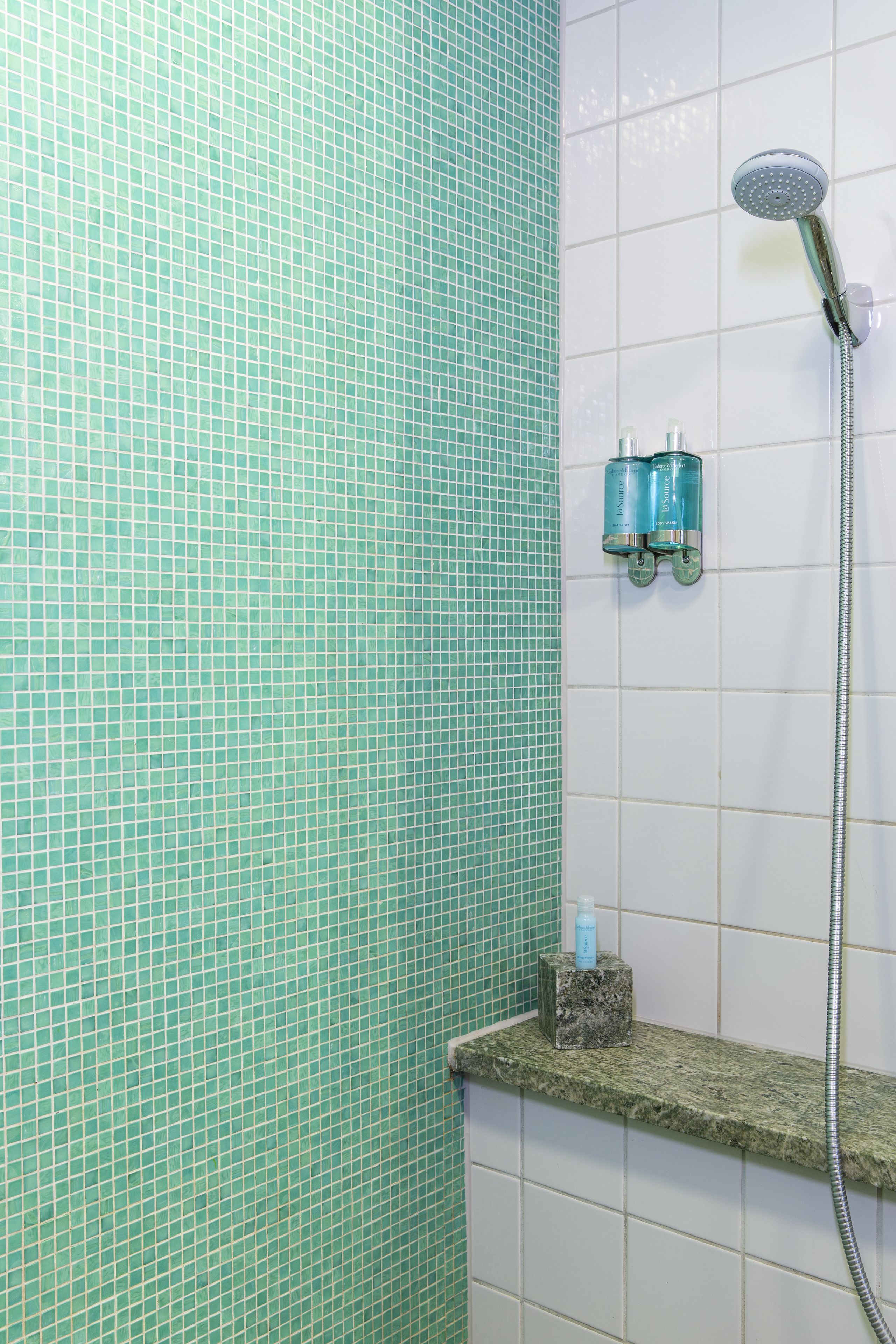 Een badkamer met een betegelde muur, een douchekop en twee shampoo flessen op een plank.