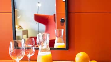 A hotel room with a table set with a newspaper, a plate of fruit, a glass of orange juice, and two empty wine glasses.
