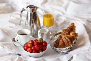 A breakfast tray with croissants, strawberries, coffee, and orange juice on a white cloth.