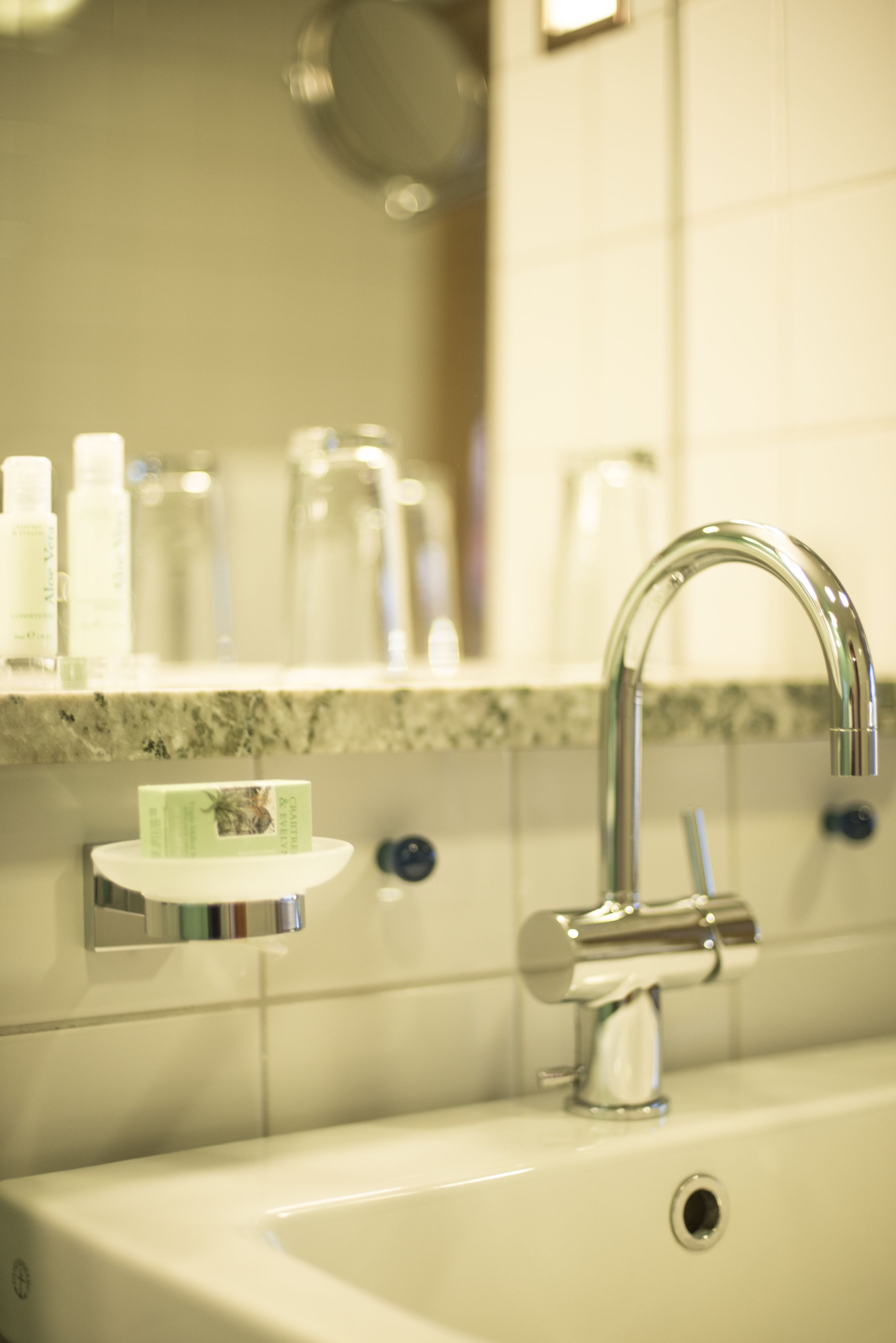 Ein Waschbecken mit chromfarbenem Wasserhahn, eine Seifenschale und ein Spiegel darüber.