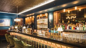 A bar area with a counter, bar stools, and a well-stocked shelf with bottles and glasses. - Hotel Rival (Stockholm)