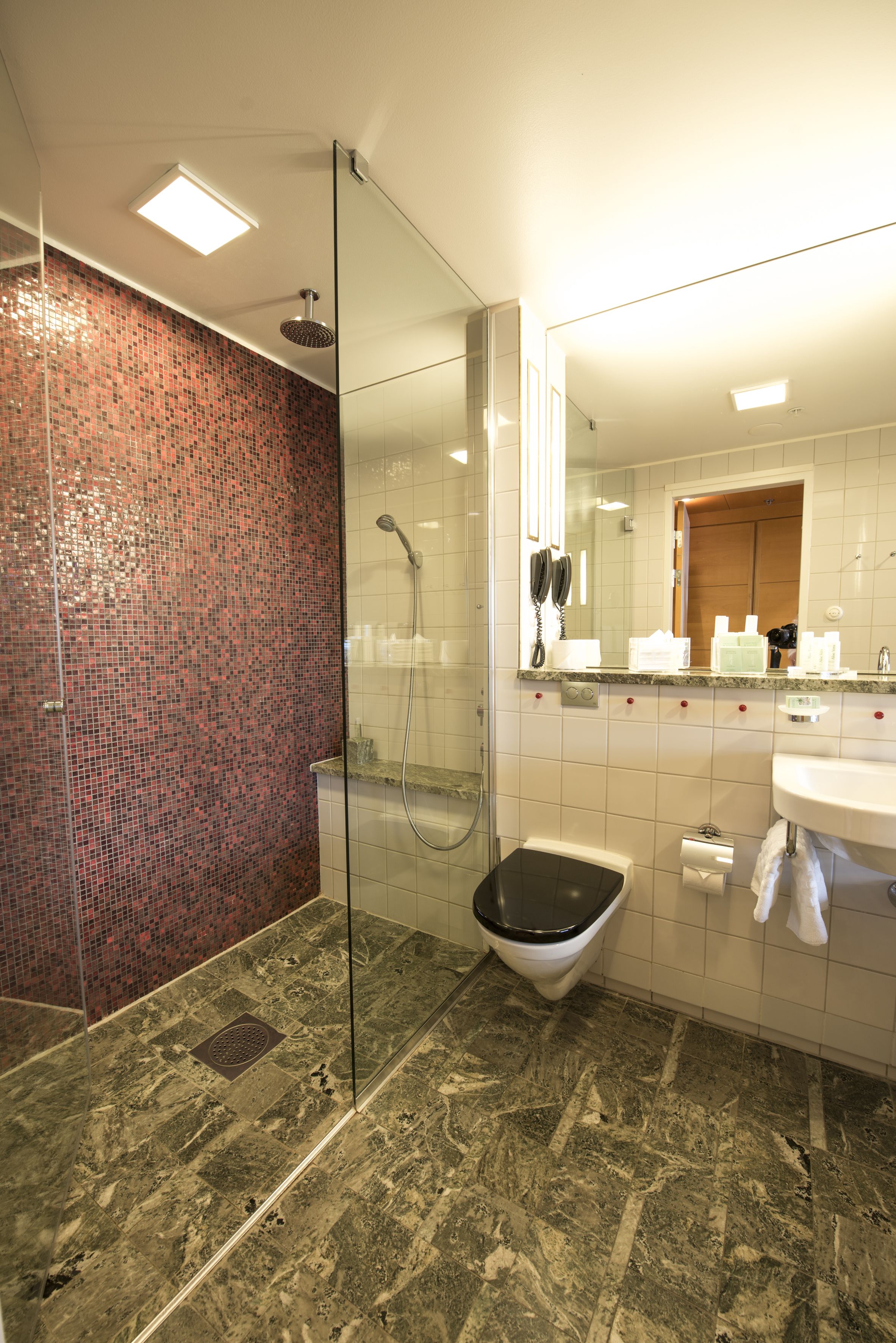 A modern bathroom with a glass-enclosed shower, a white sink, and a tiled floor.