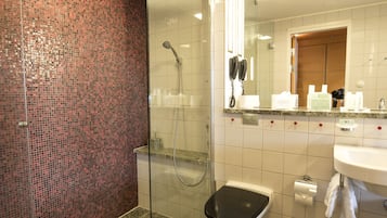 A modern bathroom with a glass-enclosed shower, a white sink, and a tiled floor.