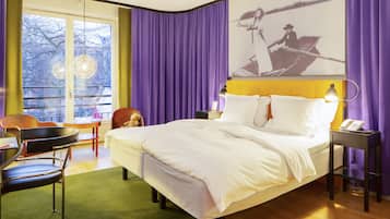 Habitación de hotel con cama, sillón, mesa, lámpara y un cuadro en la pared.