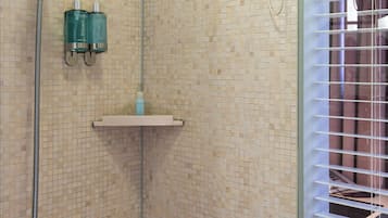 Zona de ducha con azulejos, ducha de mano, repisa de vidrio y ventana con persianas.